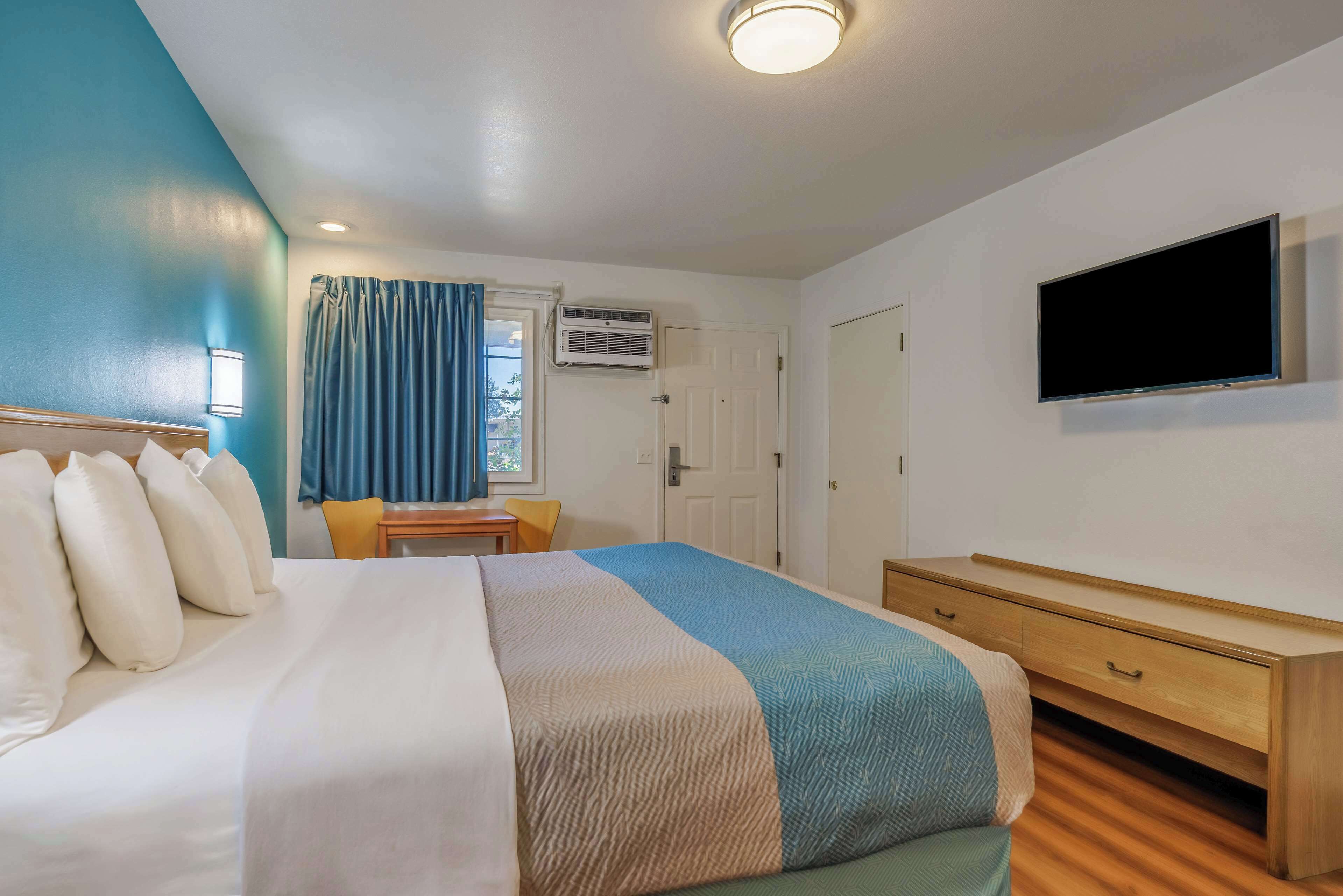 Habitación de hotel con cama, escritorio, silla, televisor y aire acondicionado.