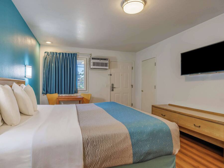 Habitación de hotel con cama, escritorio, silla, televisor y aire acondicionado.