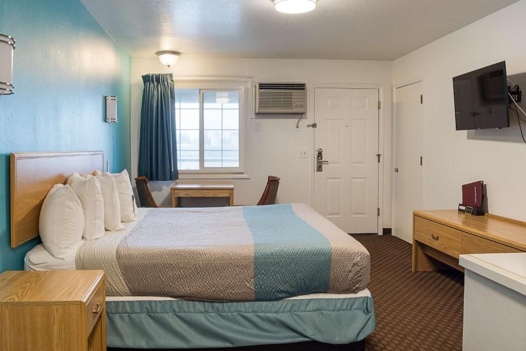 A hotel room with a bed, bedside table, desk, chair, and a television on the wall.