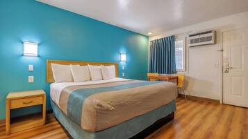 A hotel room with a bed, bedside tables, a desk, and an air conditioning unit.