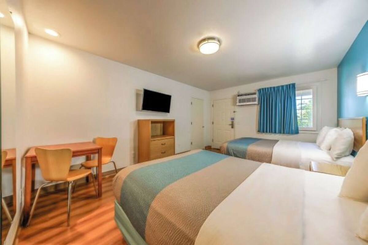 Ein Hotelzimmer mit zwei Betten, einem Schreibtisch, einem Sessel, einem Fernseher und einem Fenster mit Vorhängen.