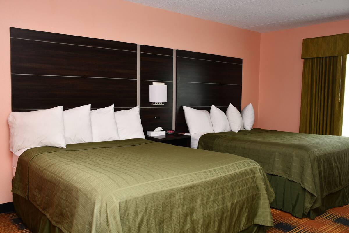 A hotel room with two beds, a nightstand, and a wall-mounted lamp.