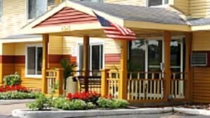 A motel with a red and white striped awning, a small porch, and a parking lot in front. - Regency Inn & Suites (Faribault)
