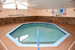 Una piscina interior con agua cristalina, una silla de salvavidas y señales de seguridad en las paredes.