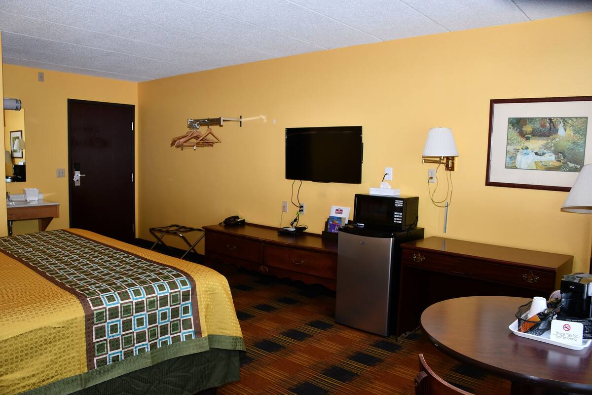 A hotel room with a bed, desk, refrigerator, and a dining table with a coffee maker.
