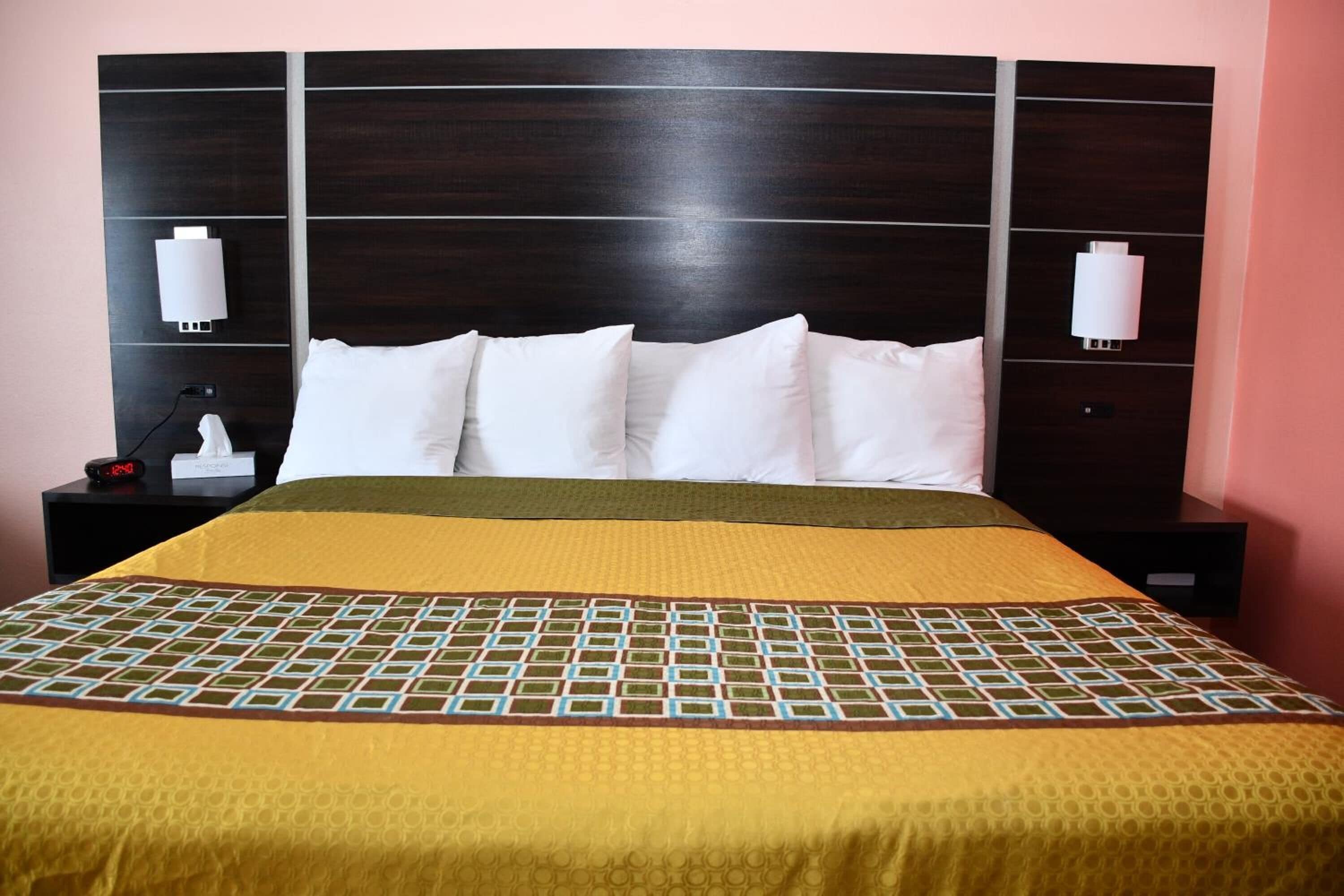 A neatly made bed with a patterned bedspread, a dark wooden headboard, and two bedside lamps.