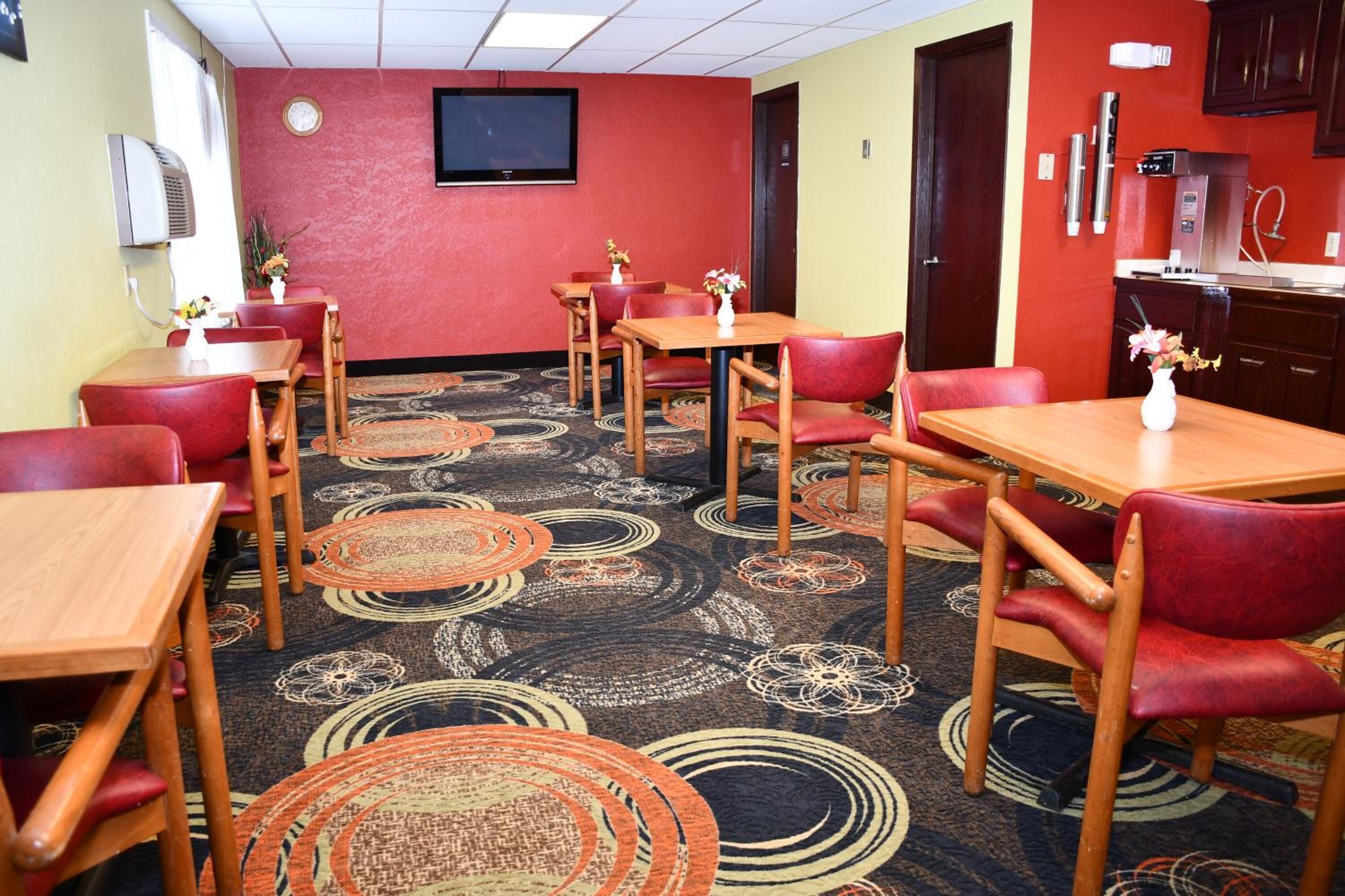 A hotel room with a carpeted floor, wooden furniture, and a kitchenette.