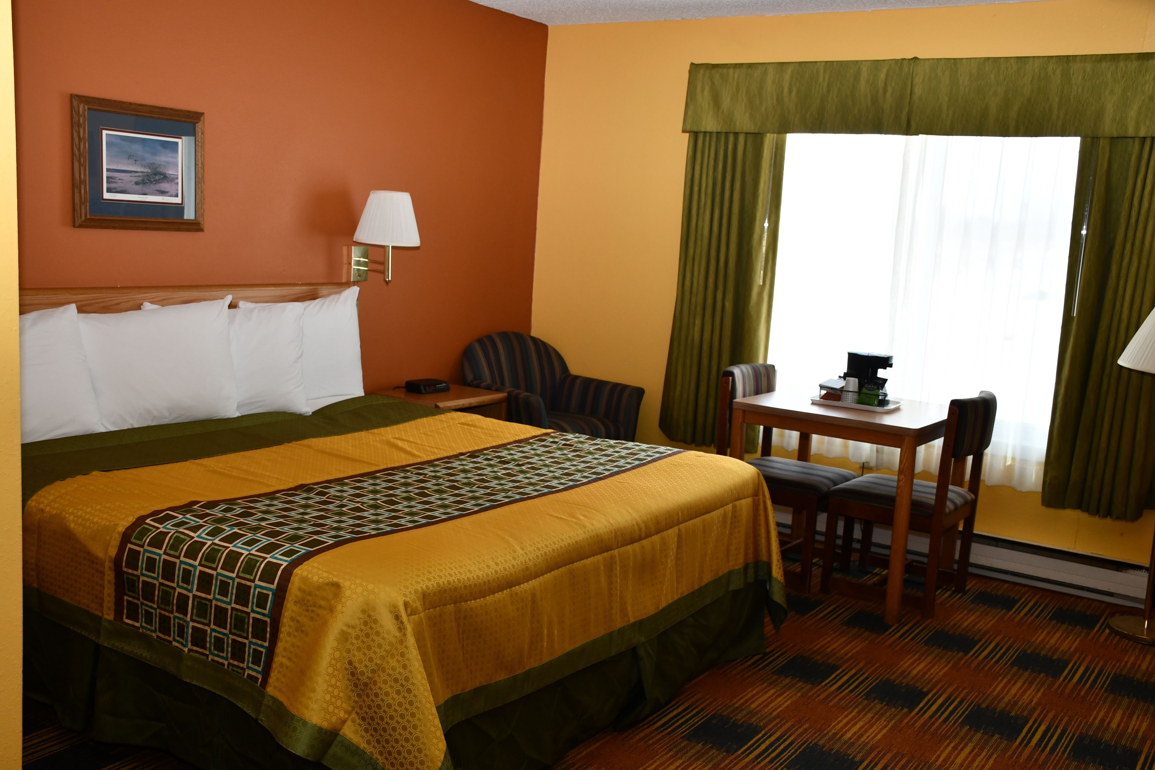 Une chambre d’hôtel avec un grand lit, un bureau avec deux chaises, une lampe et une fenêtre avec des rideaux.