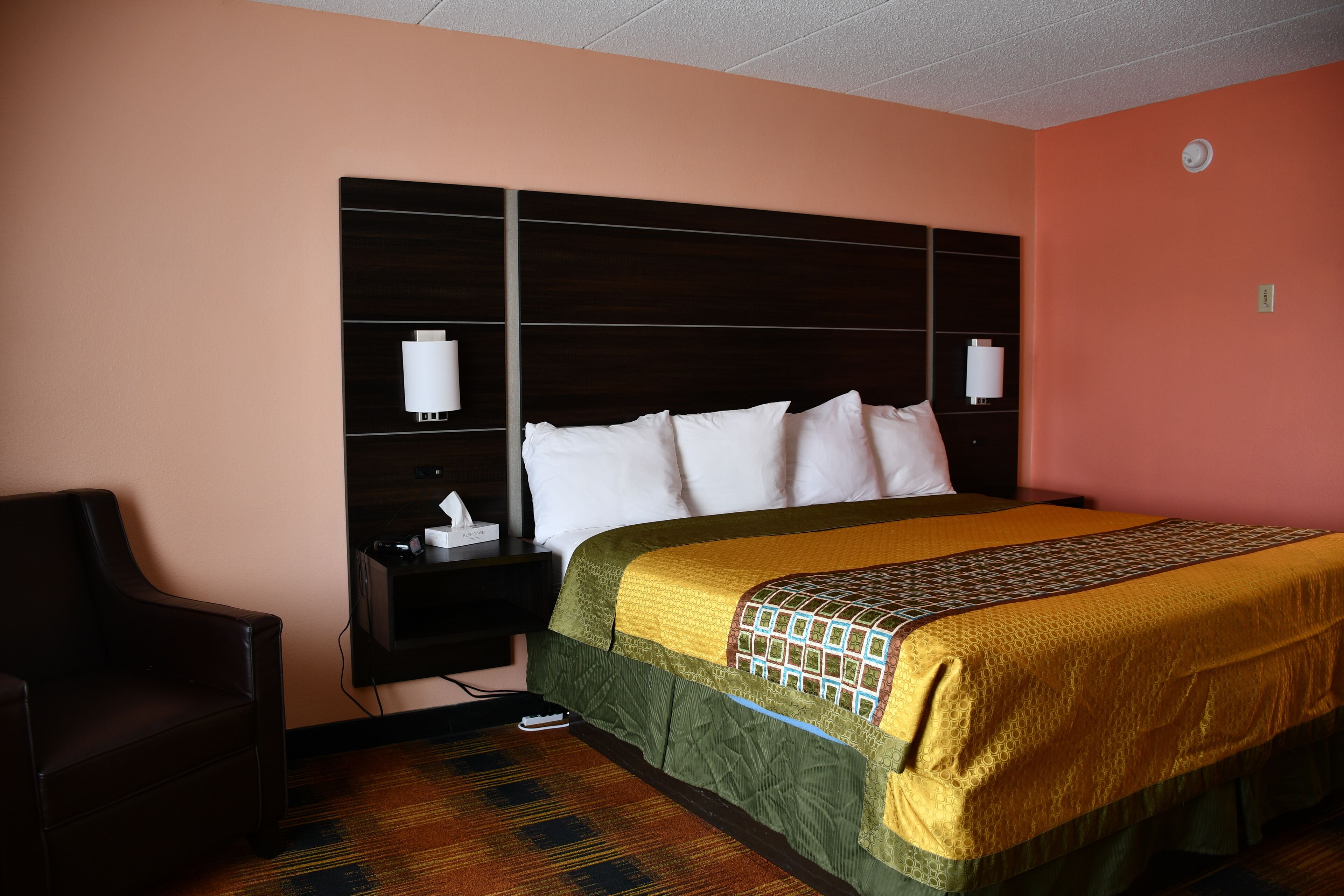 Une chambre d’hôtel avec un grand lit, une table de chevet, une chaise et une lampe fixée au mur.