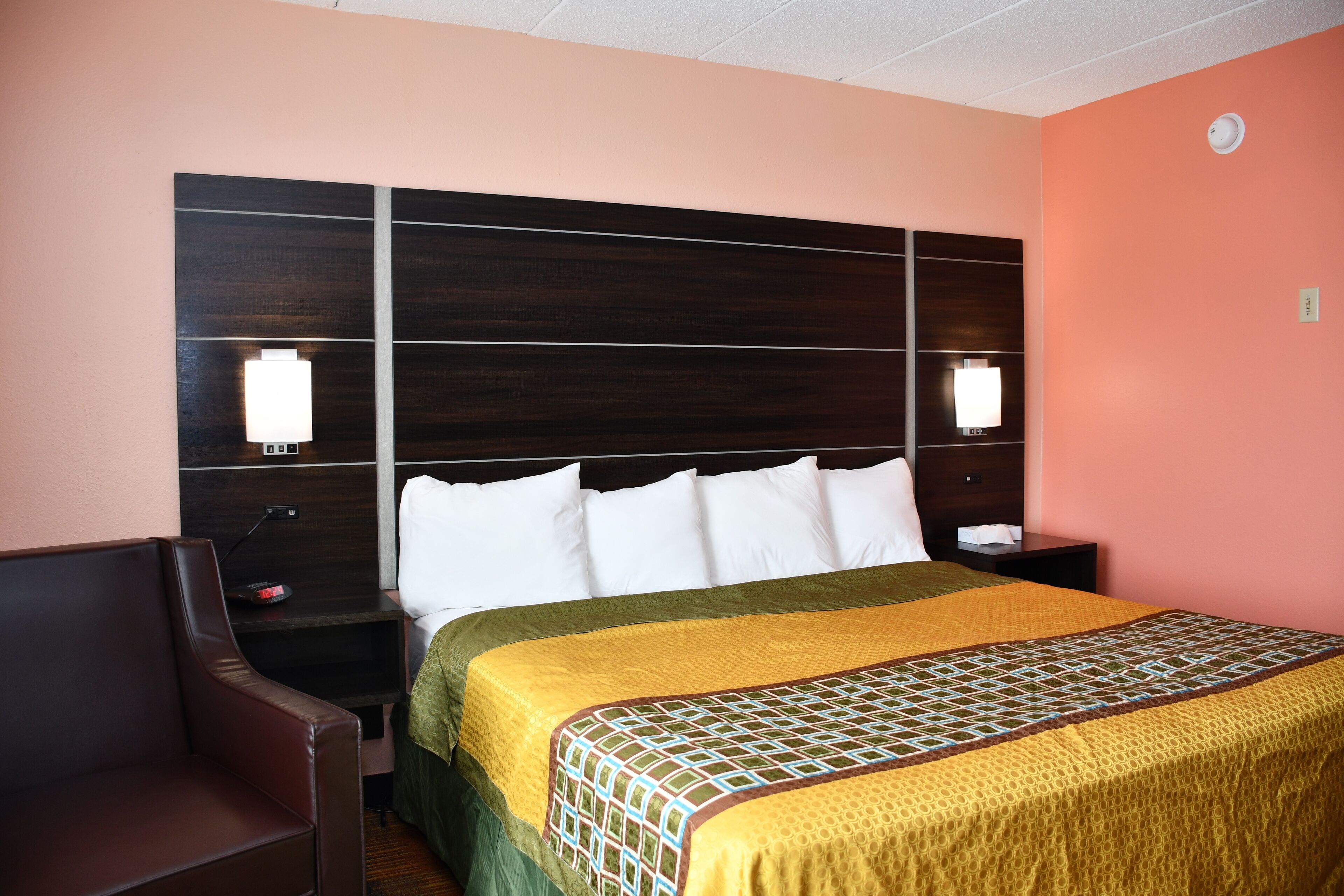 A hotel room with a large bed, a nightstand, a lamp, and a chair.