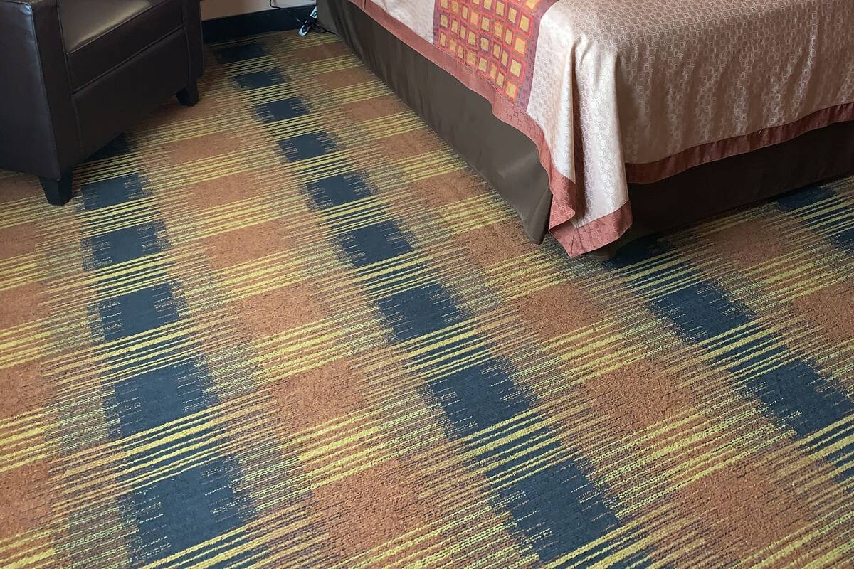 A hotel room with a large bed, two bedside tables, a chair, and a patterned carpet.