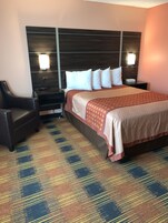 Habitación de hotel con una cama grande, dos mesitas de noche, una silla y una alfombra estampada.