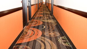 A hotel hallway with a patterned carpet, orange walls, and doors on both sides. - Regency Inn & Suites (Faribault)