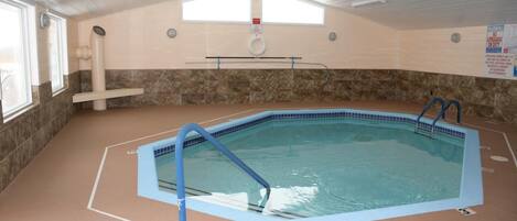 An indoor swimming pool with a blue border, a diving board, and a lifeguard sign on the wall.