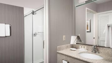 A modern bathroom with a glass shower enclosure, a granite countertop sink, and a large mirror.