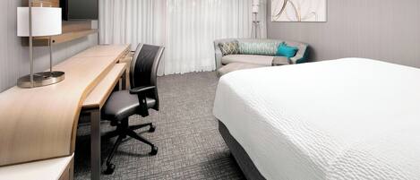 A hotel room with a bed, a desk with a chair, a flat-screen TV, a lamp, and a painting on the wall.