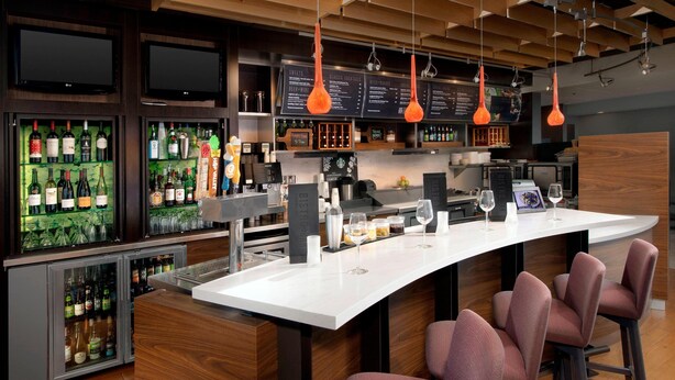 Un'area bar moderna con un bancone bianco, sgabelli da bar e una selezione di bottiglie di liquori.