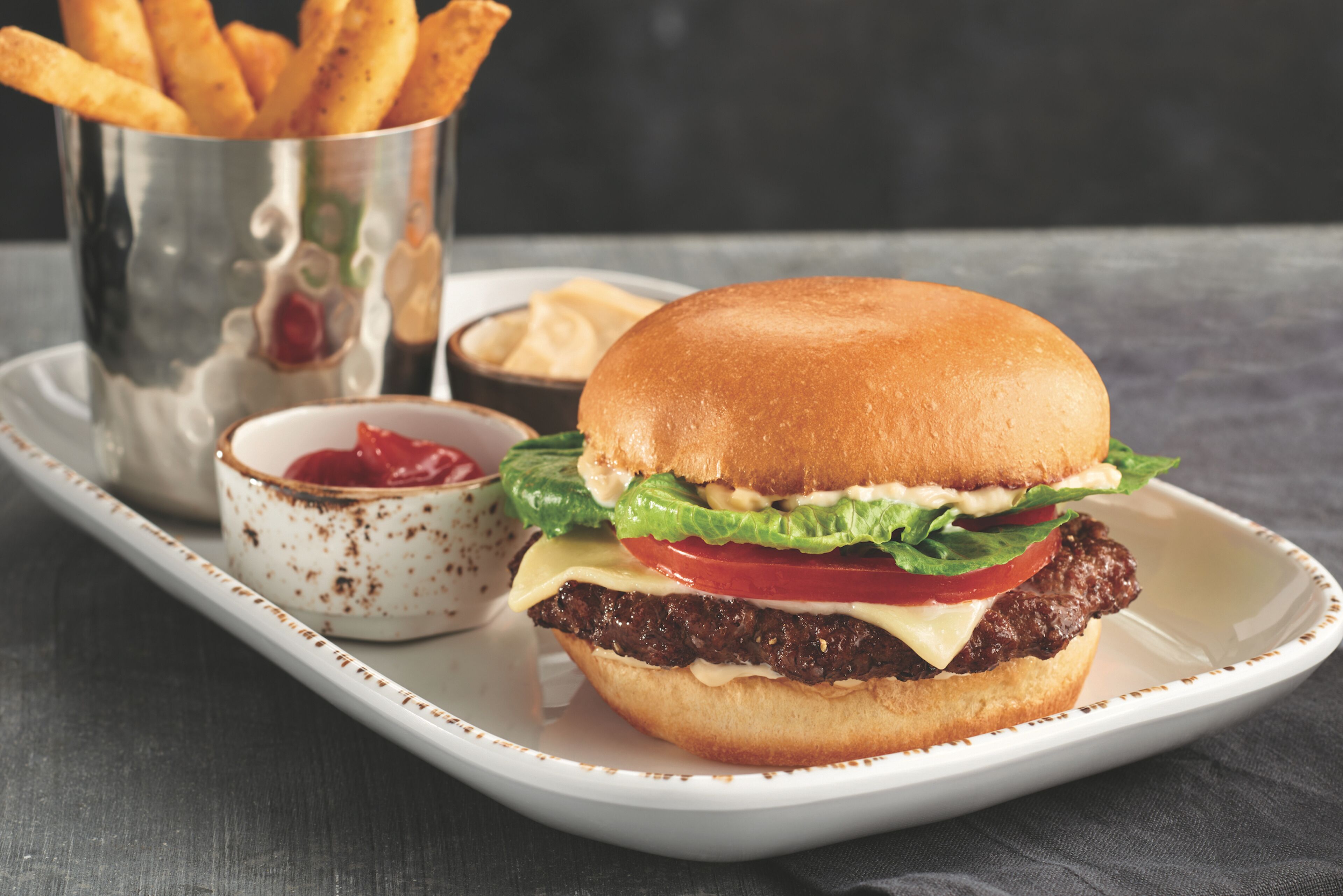 A burger with lettuce, tomato, and cheese on a bun, served with fries and ketchup.