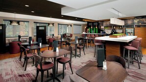 Un ristorante moderno con tavoli rotondi e banconi, una zona bar e ampie vetrate che offrono vista sull'esterno.