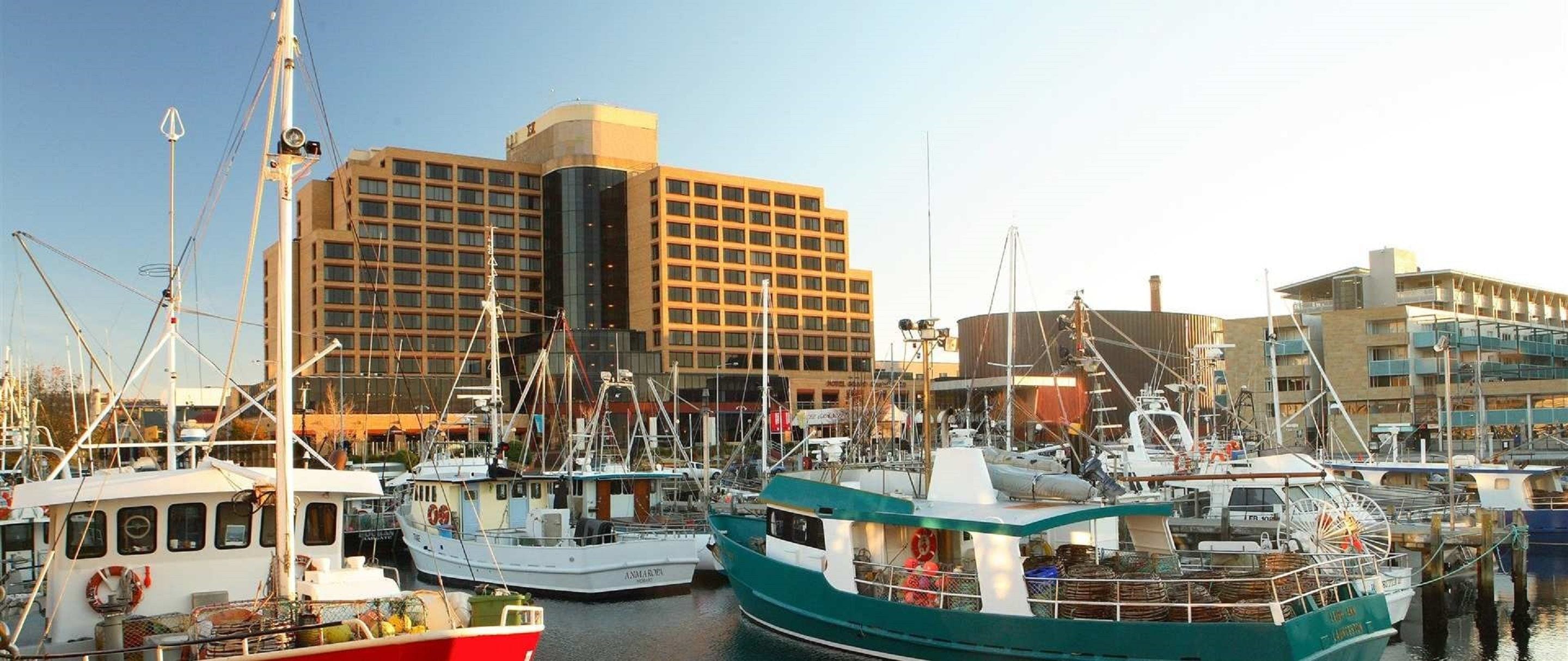 A marina with several boats docked, a large building with a modern design, and a clear sky.
