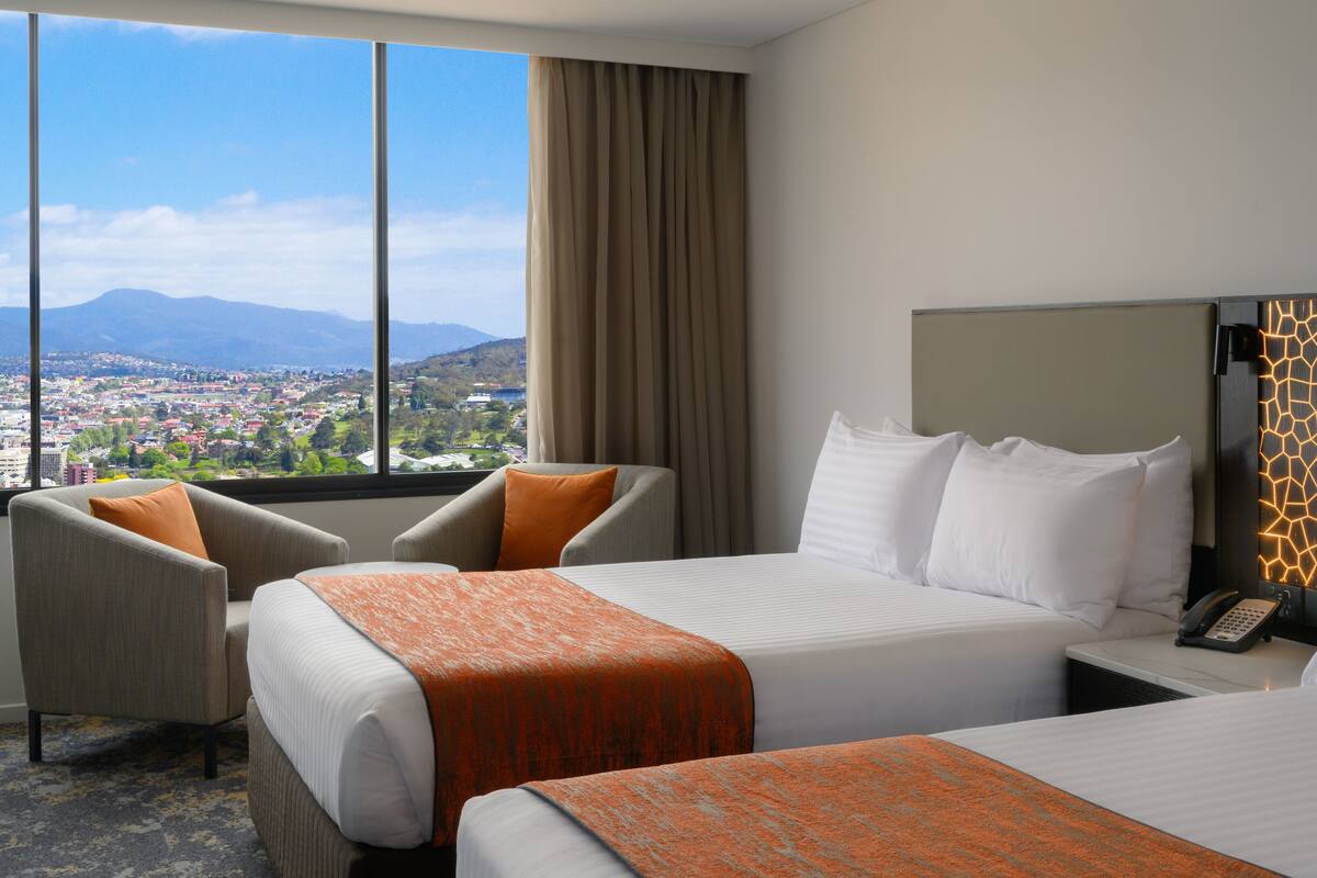 Une chambre d’hôtel avec deux lits, un canapé, une vue sur le paysage urbain et un décor mural moderne.