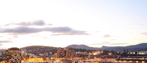 A marina with boats docked, a large building with multiple floors, and a hilly landscape in the background.