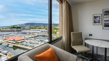 A hotel room with a large window overlooking a marina and cityscape.