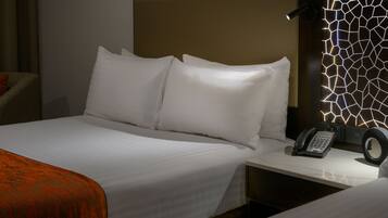 A hotel room with a neatly made bed, a bedside telephone, and a wall with a geometric light pattern.