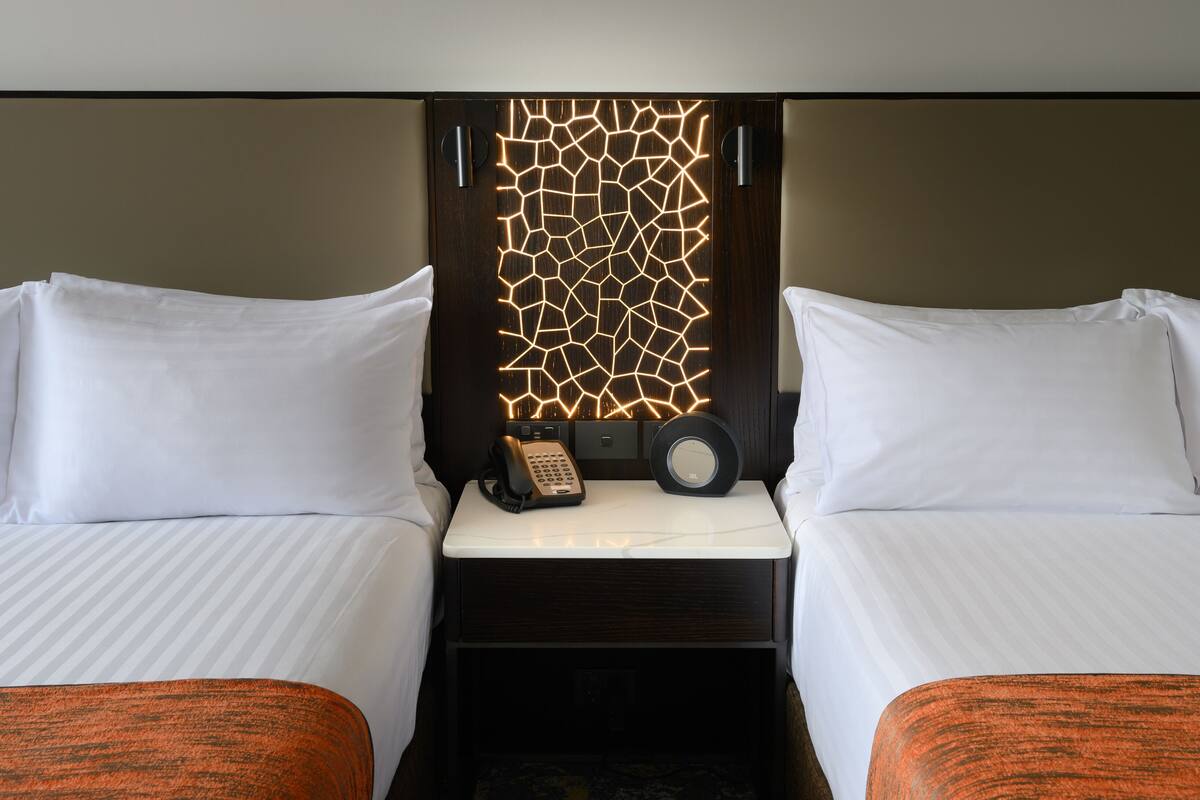 Une chambre d’hôtel avec deux lits, une table de chevet avec un téléphone et un panneau décoratif au mur.