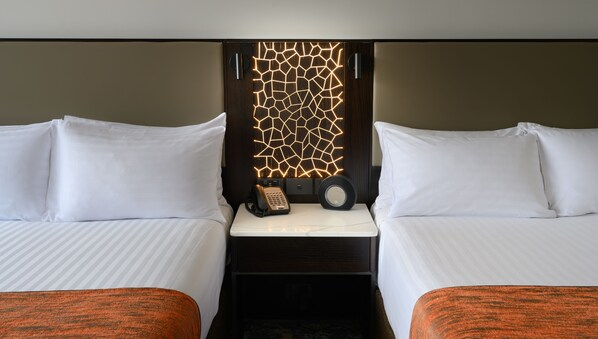 Habitación de hotel con dos camas, una mesita de noche con teléfono y un panel decorativo en la pared.