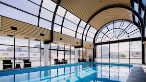 Una amplia piscina cubierta con techo curvo y grandes ventanales que ofrecen vistas de la ciudad.