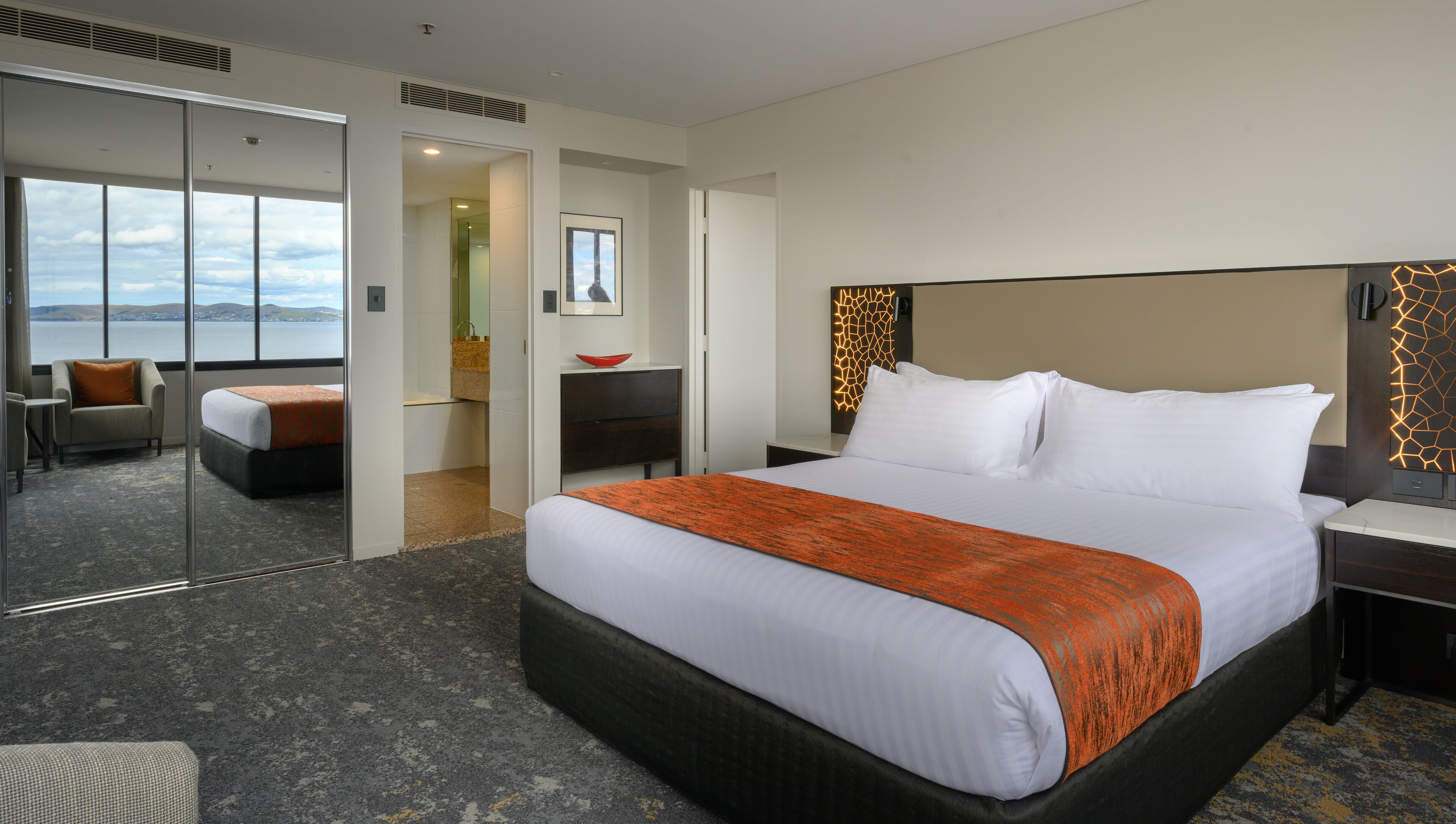 A hotel room with a large bed, a desk, a chair, and a view of the water.