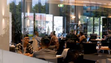 An indoor dining area with tables and chairs, large windows, and a view of the outside.