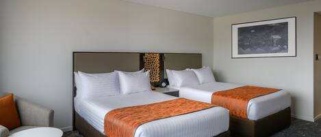 Habitación de hotel con dos camas, un sofá, una mesita y un cuadro en la pared.
