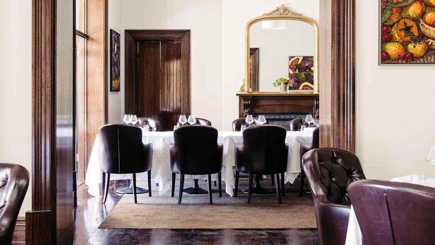 Un coin repas avec une table dressée pour quatre personnes, un miroir et une nature morte représentant des fruits accrochée au mur.