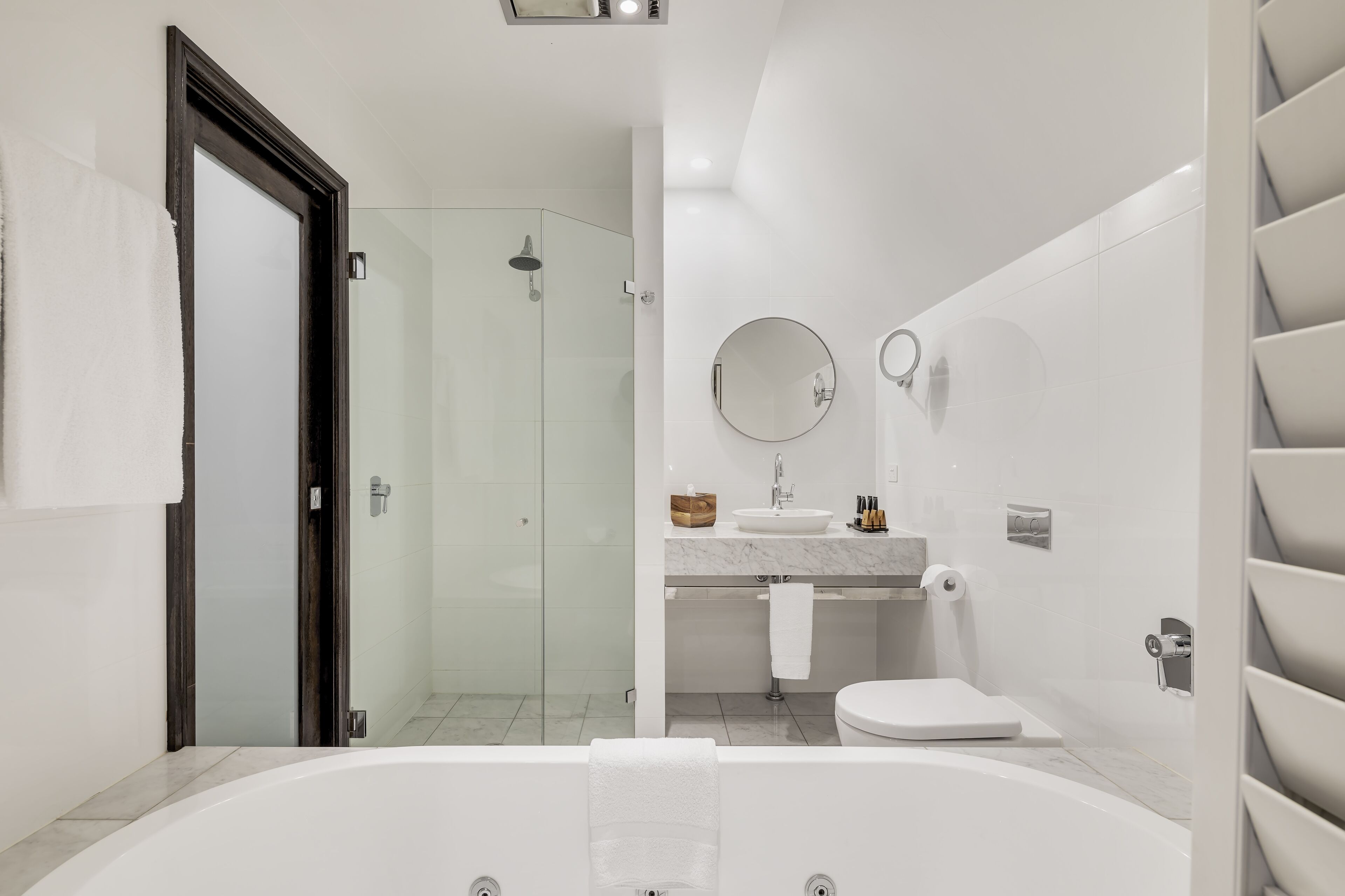Et moderne badeværelse med brusekabine i glas, et fristående badekar, en vask med spejl og et toilet.