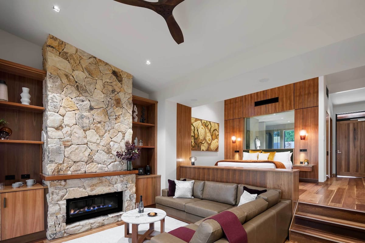 A modern living room with a stone fireplace, wooden furniture, and a large mirror.