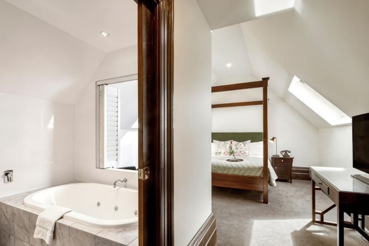 A bedroom with a four-poster bed, a skylight, and a large window.