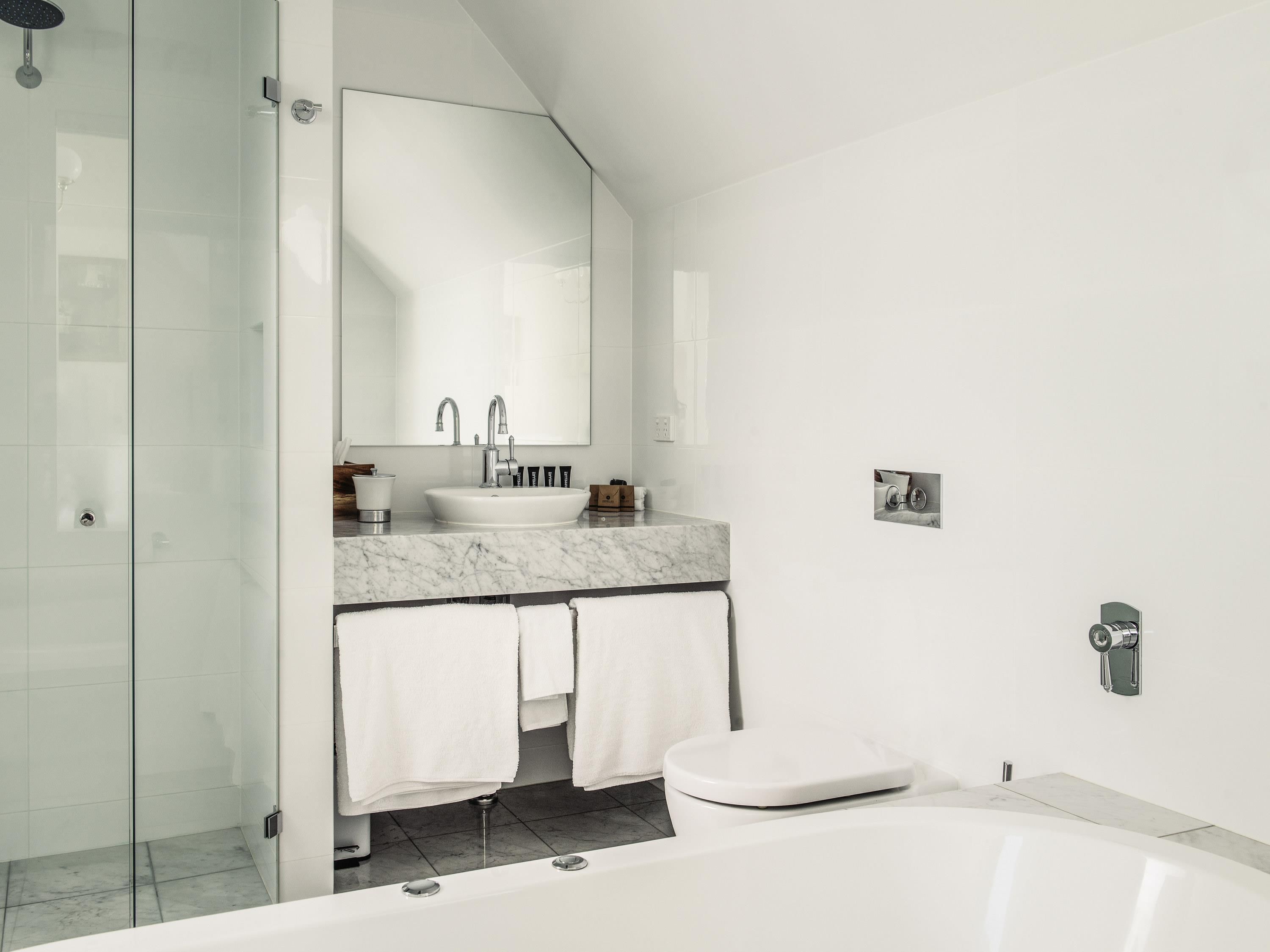 A modern bathroom with a glass shower enclosure, a white sink with a marble countertop, a toilet, and a bathtub.