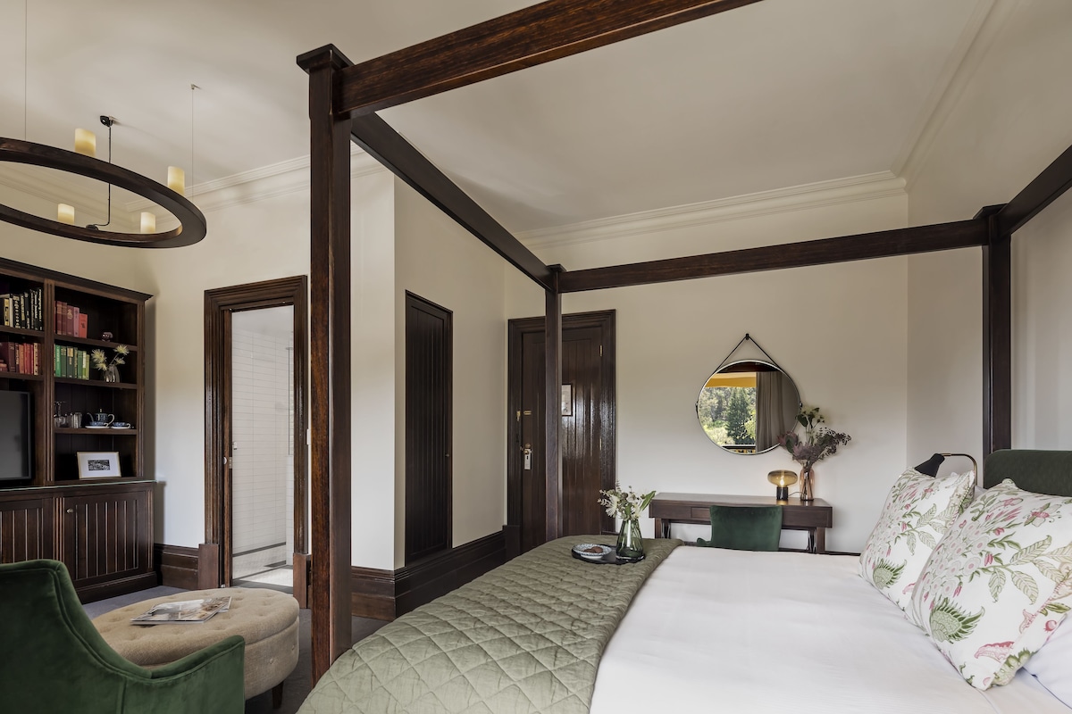 A bedroom with a large bed, a wooden ceiling, a bookshelf, and a desk with a mirror.