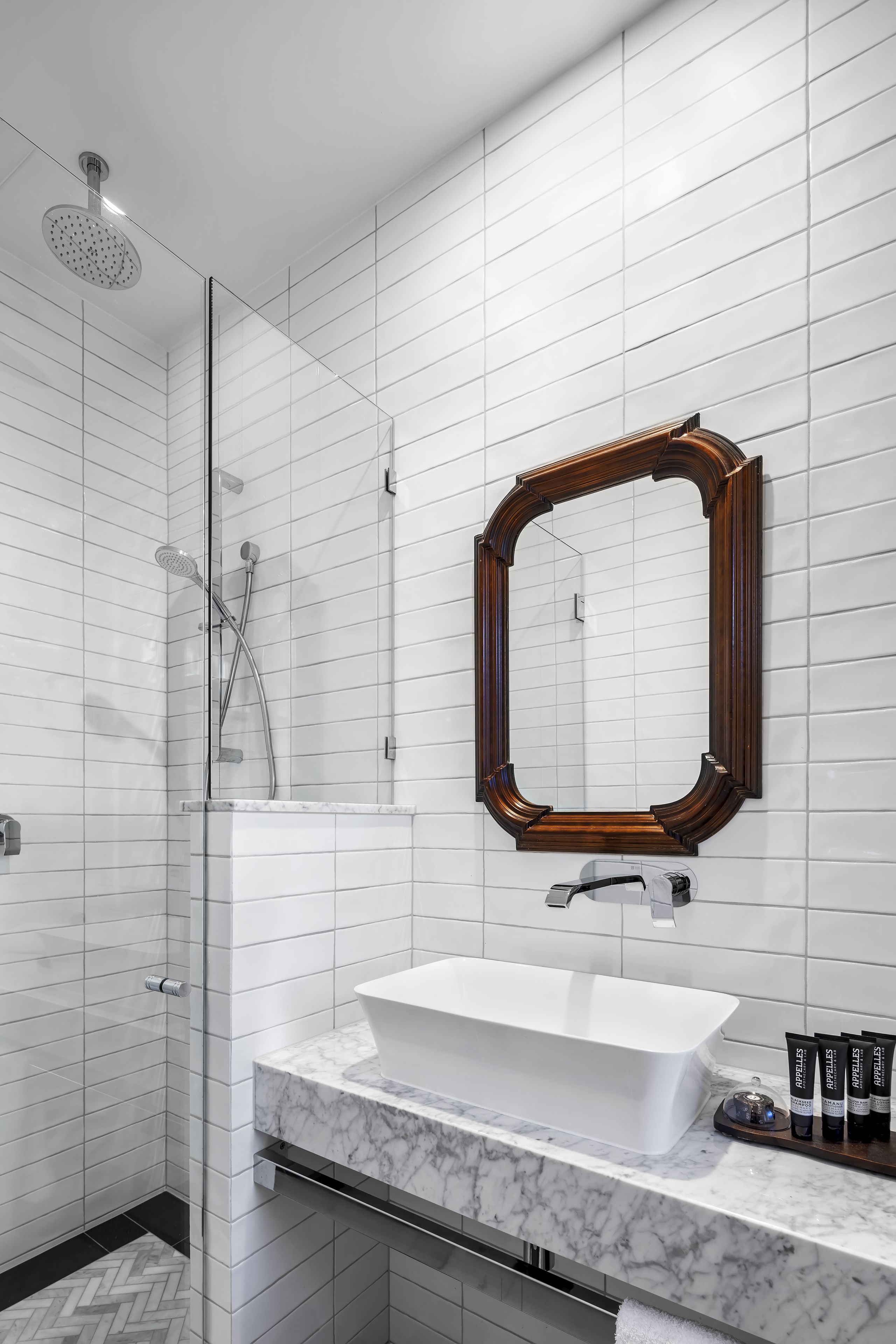 Un baño moderno con un espejo grande, azulejos blancos, una bañera independiente y una zona de ducha.