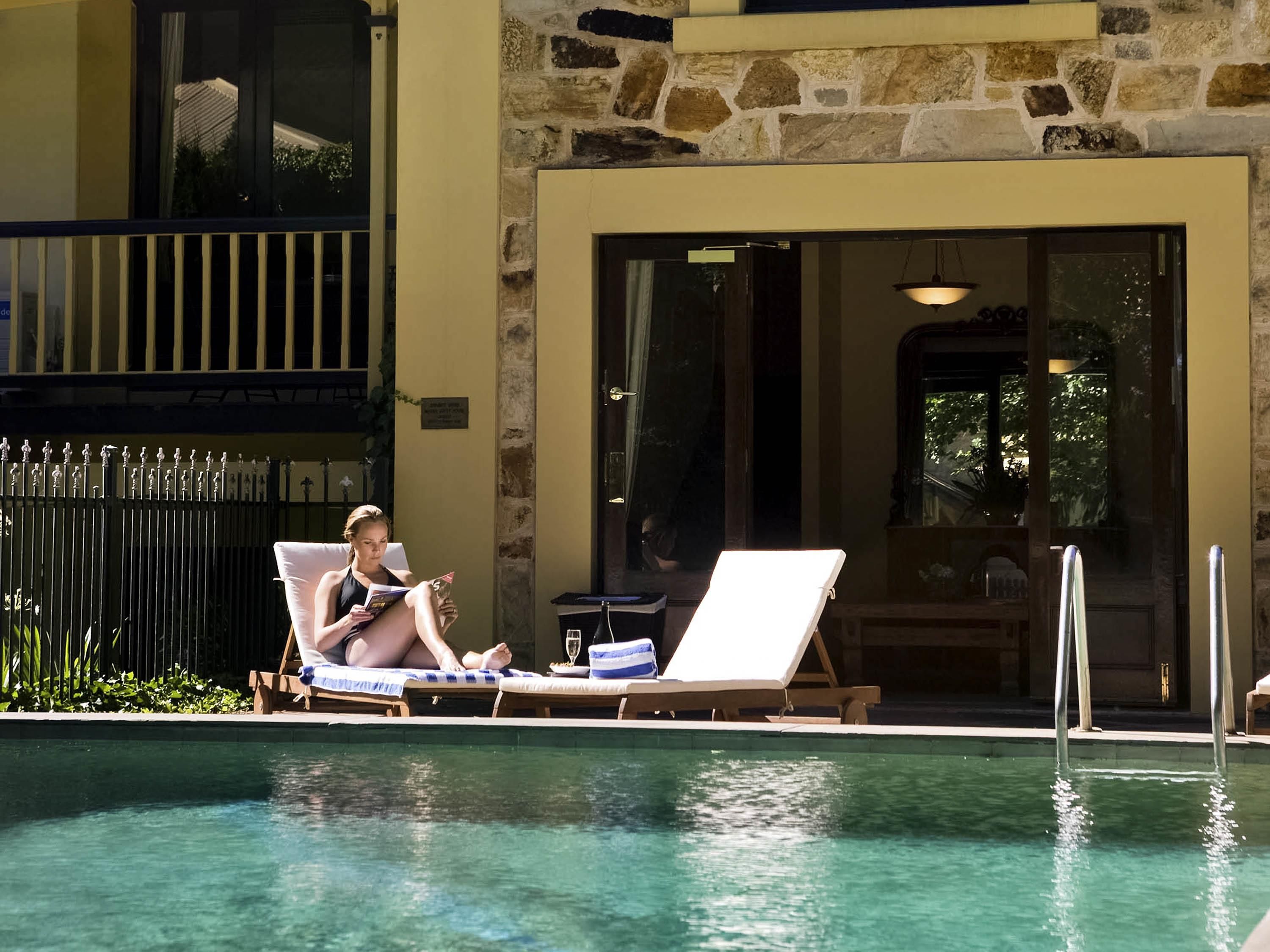 A poolside area with lounge chairs and a person reading a book.