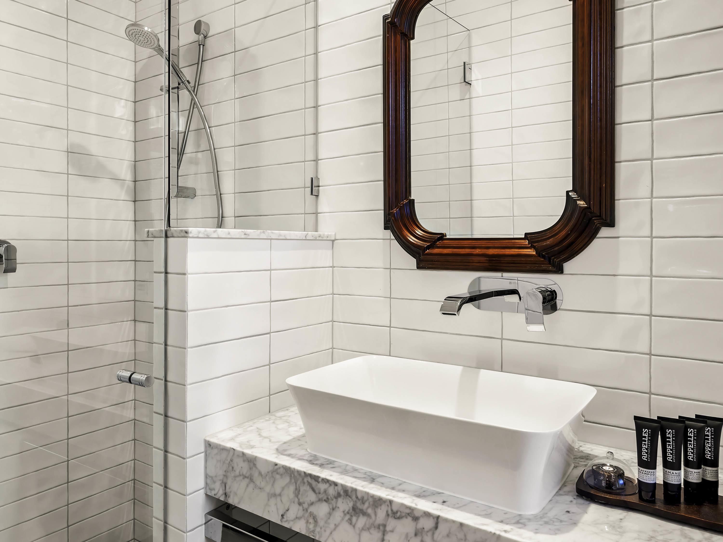 A bathroom with a white subway tile wall, a large mirror, a white sink, and a shower area.