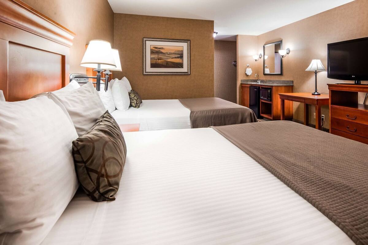 A hotel room with two beds, a desk, a television, a mirror, and a painting on the wall.