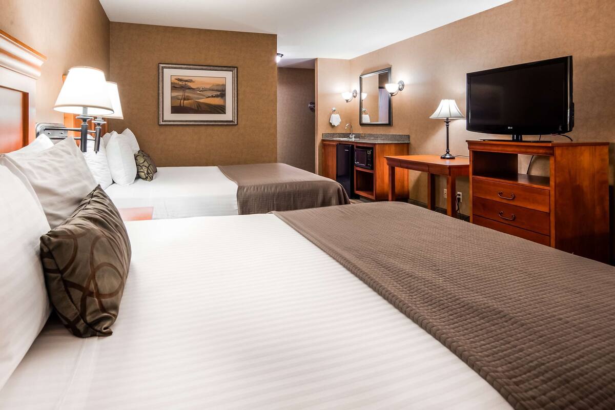 A hotel room with two beds, a desk, a television, and a painting on the wall.