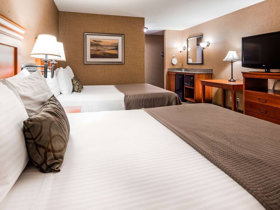 A hotel room with two beds, a desk, a television, and a painting on the wall.