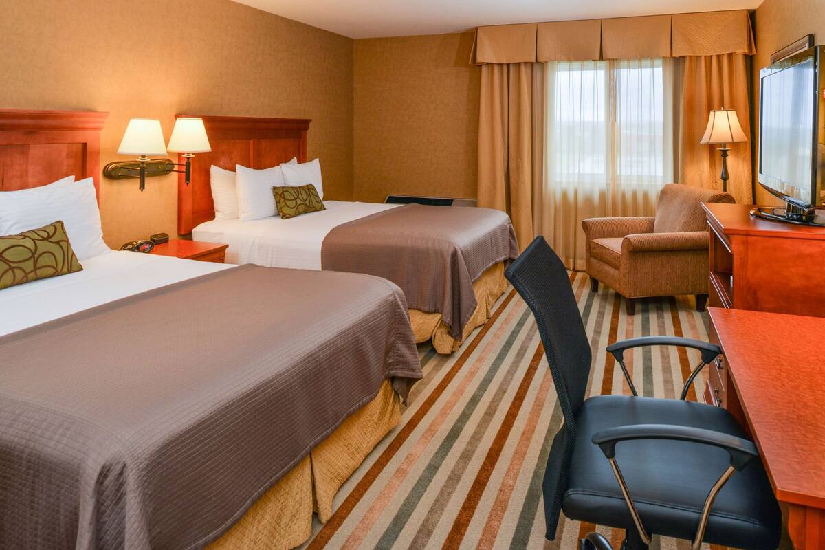 A hotel room with two beds, a desk, a chair, and a television.