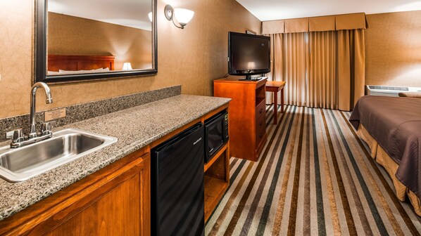 A hotel room with a kitchenette, a bed, a television, and a bathroom.