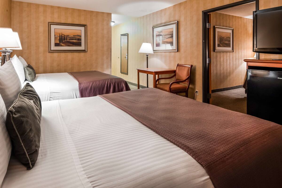 A hotel room with two beds, a desk, a chair, a television, and framed artwork on the walls.