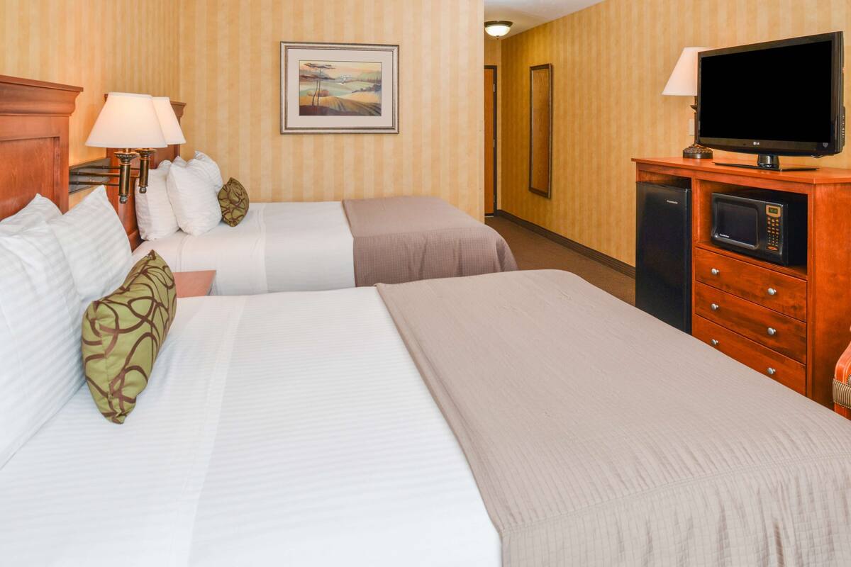 A hotel room with two beds, a television, a microwave, and a painting on the wall.